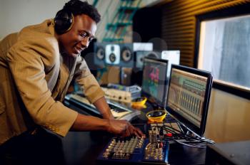 Male dj in headphones listening a record at mixing consol, recording studio interior on background. Synthesizer and audio mixer, musician workplace, creative process