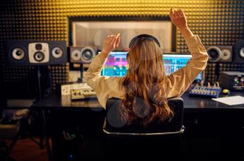 Female sound engineer at mixing consol, back view, recording studio interior on background. Synthesizer and audio mixer, musician workplace, creative process