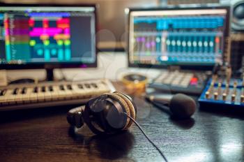 Headphones on the table, recording studio interior on background. Synthesizer, audio mixer and monitors, sound engineer workplace