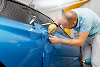 Protective vinyl foil or film installation process, car wrapping. Worker makes auto detailing. Automobile paint protection, professional tuning