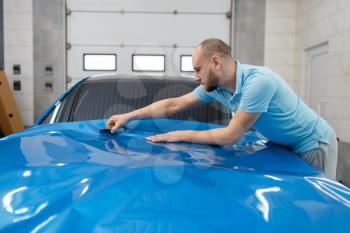 Male car wrapper installs protective vinyl foil or film on vehicle hood. Worker makes auto detailing. Automobile paint protection coating, professional tuning