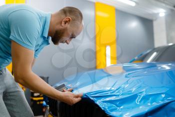 Male car wrapper puts protective vinyl foil or film on hood. Worker makes auto detailing. Automobile paint protection coating, tuning