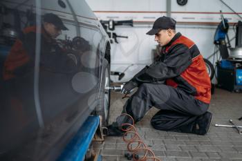Mechanic with pneumatic wrench unscrews the wheel in tire service. Man repairs car tyre in garage, automobile inspection in workshop