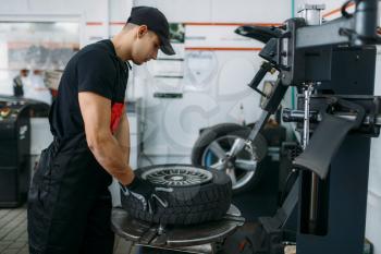 Mechanic fixing broken wheel on tire fitting machine, repairing service. Man repairs car tyre in garage, automobile inspection in workshop