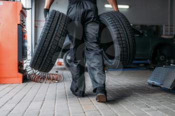 Auto mechanic holds two new tires, repairing service. Worker repairs car tyre in garage, professional automobile inspection in workshop