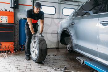 Auto mechanic in uniform holds wheel, tire service. Worker repairs car tyre in garage, professional automobile inspection in workshop