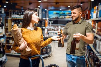 Attractive couple choosing alcohol in grocery supermarket. Man and woman with cart buying beverages in market, customers shopping food and drinks