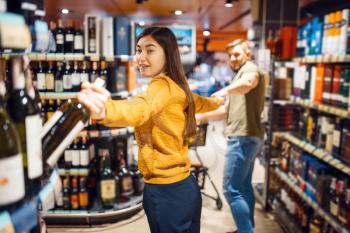 Funny couple in grocery store, alcohol department. Man and woman with cart buying beverages in market, customers shopping food and drinks