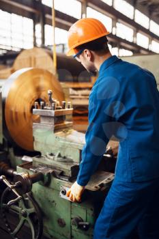 Turner in uniform and helmet works on lathe, factory. Industrial production, metalwork engineering, power machines manufacturing