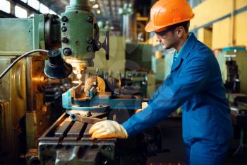 Turner in uniform and helmet works on lathe, plant. Industrial production, metalwork engineering, power machines manufacturing