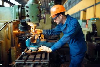 Male technician in uniform and helmet works on lathe, plant. Industrial production, metalwork engineering, power machines manufacturing