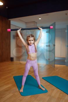 Little girl doing exercise with bar on mat in gym, fitness workout. Female kid in sportswear, child on training in sport club