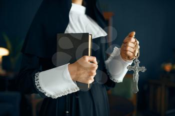 Young nun in a cassock with a cross around her neck holds a book. The sister is preparing for pray in the monastery