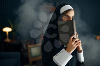 Young nun in a cassock holds a book. The sister is preparing for prayer in the monastery, religion and faith, religious people