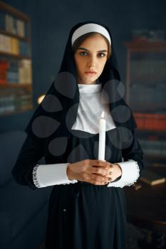 Young nun in a cassock holds a candle. The sister is preparing for prayer in the monastery, religion and faith, religious people