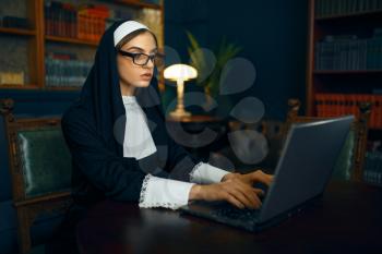 Young nun in a cassock and glasses works on laptop. The sister in the monastery, religion and faith, religious people
