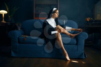 Sexy nun in a cassock paints her toenails with nail polish, vicious desires. Corrupt sister in the monastery, sinful religious people, attractive sinner
