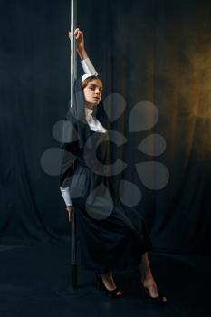 Sexy nun in a cassock dances on a pole like a stripper, vicious desires. Corrupt sister in the monastery, sinful religious person, attractive sinner