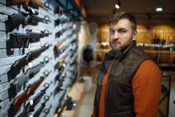 Man looking on handguns on showcase in gun shop. Euqipment for hunters on stand in weapon store, hunting and sport shooting hobby