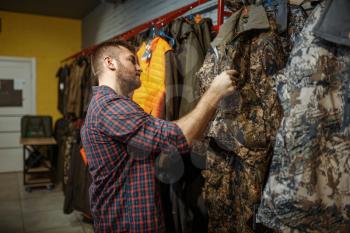 Man choosing uniform on showcase in gun shop. Euqipment and rifles for hunters on stand in weapon store, hunting and sport shooting hobby