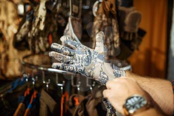 Man choosing gloves for hunters on showcase in gun shop. Euqipment and rifles on stand in weapon store, hunting and sport shooting hobby