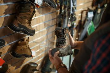 Man choosing boots for hunters at showcase in gun shop. Euqipment and rifles on stand in weapon store, hunting and sport shooting hobby