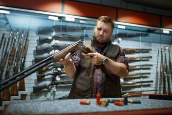 Man looks on rifle barrel at counter in gun shop. Euqipment for hunters on stand in weapon store, hunting and sport shooting hobby