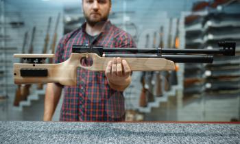 Male person shows pneumatic rifle at showcase in gun shop. Euqipment for hunters on stand in weapon store, hunting and sport shooting hobby