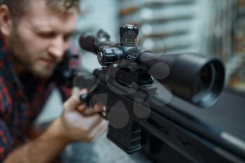 Man checks optical sight on sniper rifle in gun shop. Euqipment for hunters on stand in weapon store, hunting and sport shooting hobby