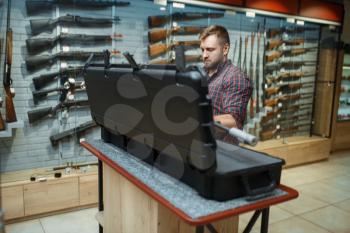 Man takes sniper rifle from the case in gun shop. Euqipment for hunters on stand in weapon store, hunting and sport shooting hobby