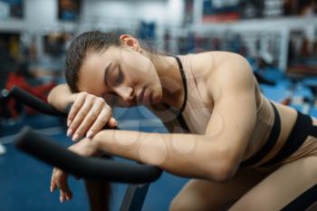 Tired woman sleeps on a stationary bike in gym. People on fitness workout in sport club, athletic girls in sportswear on training indoors