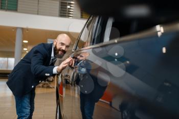 Man checks the paintwork of new automobile in car dealership. Customer in vehicle showroom, male person buying transport, auto dealer business