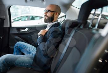 Man checks the comfort of rear seats in new automobile, car dealership. Customer in vehicle showroom, male person buying transport, auto dealer business