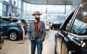 Man in a cowboy hat choosing new automobile in car dealership. Customer in vehicle showroom, male person buying transport, auto dealer business