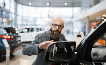 Man checks the paintwork of new pickup truck in car dealership. Customer in vehicle showroom, male person buying transport, auto dealer business