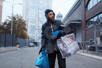 Bearded tramp man with bag on city street. Poverty is a social problem, homelessness and loneliness, alcoholism and drunk addiction, urban lonely
