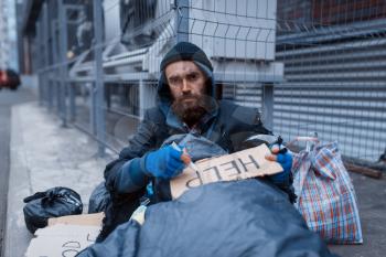 Bearded dirty homeless writes help sign on city street. Poverty is a social problem, homelessness and loneliness, alcoholism and drunk addiction, urban lonely