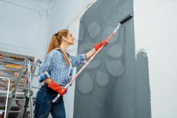 Female house painter in gloves paints the wall. Home repair, laughing woman doing appartment renovation, room decoration renovating