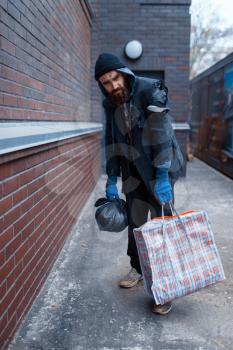Homeless man with bag on city street. Poverty is a social problem, homelessness and loneliness, alcoholism and drunk addiction, urban lonely