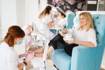 Two women on pedicure procedure in beauty salon. Professional beauticians and female customers, toenail care in spa studio