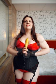 Fat perverse woman in erotic lingerie holds banana. Sexy overweight girl with big breast, corrupt large size lady