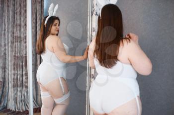 Fat depraved woman poses at the mirror in erotic bunny costume. Sexy overweight girl with big breast, perverse large size lady