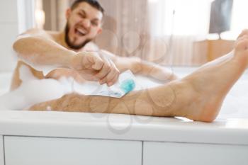 Man removes hair on legs in bath with foam, morning hygiene, waxing depilation. Male person resting in bathroom, skin and body treatment procedures