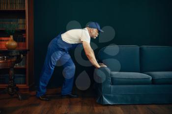 Elderly cargo man in uniform moves sofa in home office. Adult delivery worker, deliver in cap holds couch indoors, delivering service or business