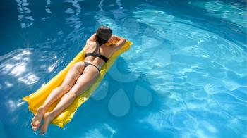 Slim woman sunbathing on inflatable mattress in the pool on resort. Beautiful girl relax at the poolside in sunny day, summer holidays of attractive female person