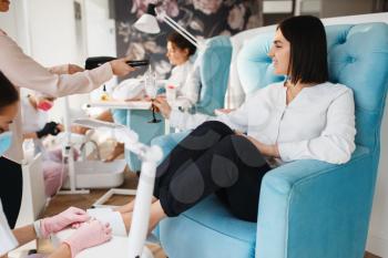 Two women with champagne, pedicure procedure in beauty salon. Professional beauticians and female customers, toenail care in spa studio