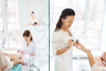 Manicure masters applies nail polish to woman, beauty salon. Professional beautician and female customer, fingernail care in spa studio