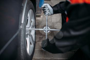 Mechanic in uniform unscrews the wheel in tire service. Man repairs car tyre in garage, automobile inspection in workshop
