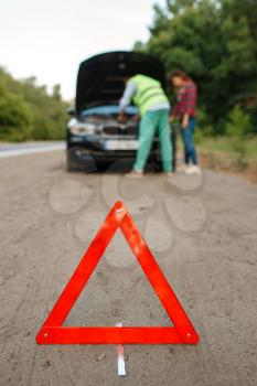 Emergency stop sign, young couple at the opened hood on road, car breakdown. Broken automobile or emergency accident with vehicle, trouble with engine on highway