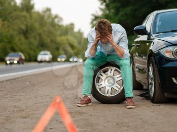 Car breakdown, tired man sitting on spare tyre. Broken automobile or problem with vehicle, trouble with punctured auto tire on highway, emergency stop sign